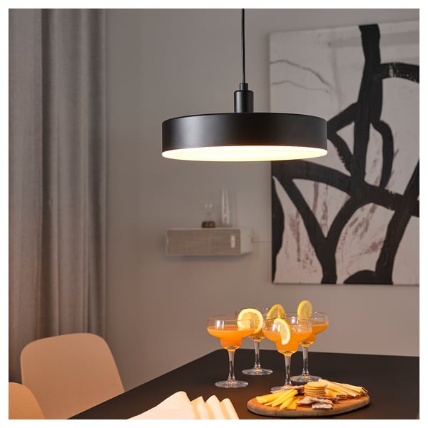 Modern dining setup with black NYMÅNE pendant light, orange drinks, and hors doeuvres on a table with an abstract painting in the background.