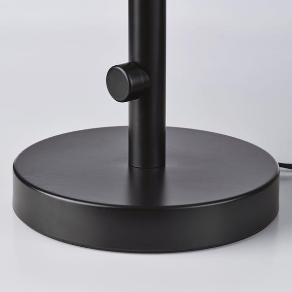 Modern floor lamp with weighted base, metal rod, and dial-like control for stability and light adjustment.