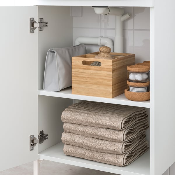 A bathroom cabinet holds folded towels, a wooden box, and round cork organisers, providing organised storage.