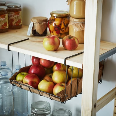 Wooden shelves with hanging produce baskets and jars of preserved foods, utilising vertical storage space efficiently.