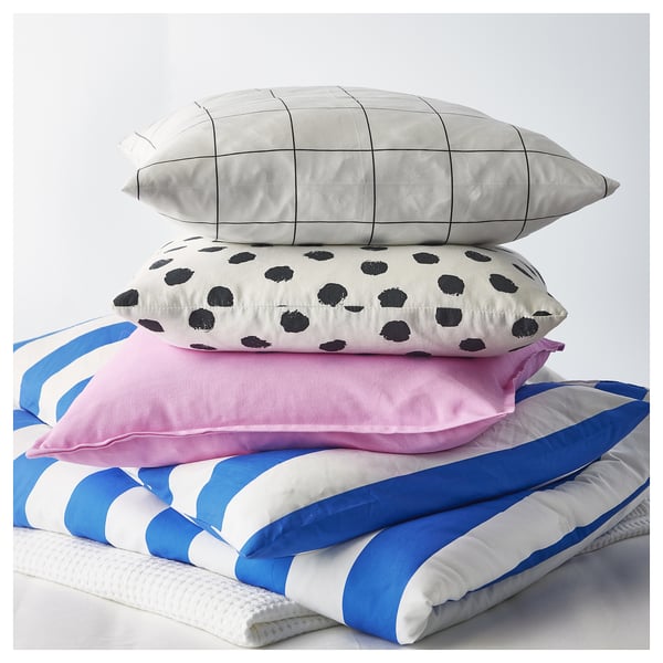 Four cushions stacked: top with black dots on white, grey grid pattern, pink, blue and white stripes.