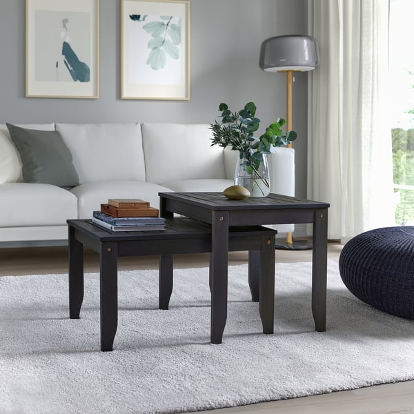 Modern black, nested acacia wood tables, compact size, white couch, grey rug, leafy prints.