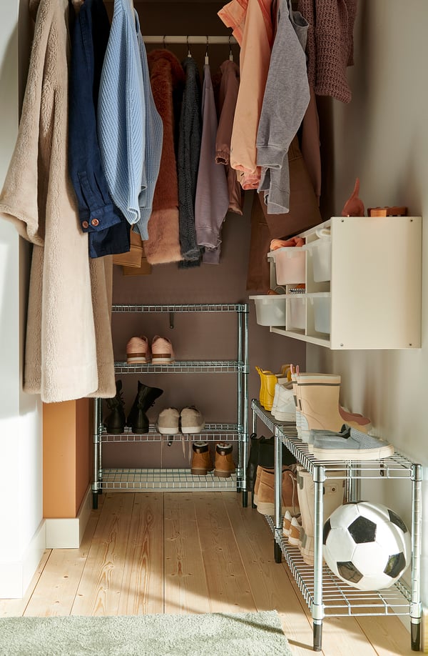 Closet with hanging clothes, shelving units filled with shoes, boxes, and a football ball. Wooden floor, white walls. Efficient storage solution.