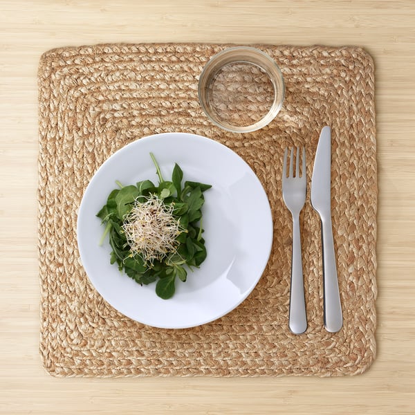 Table set with OMBONAD square jute place mat, white plate, greens, glass, fork & knife.