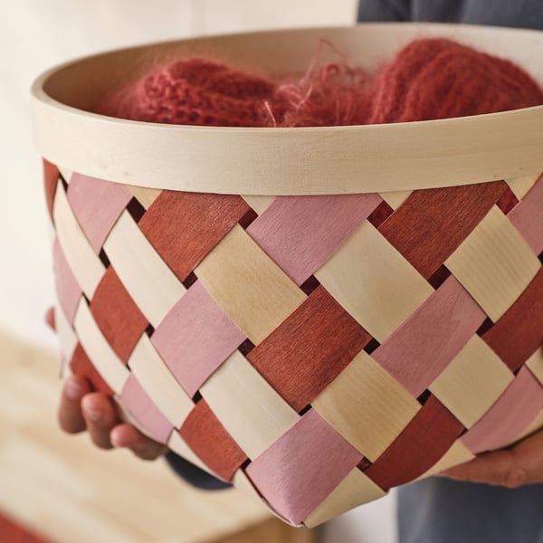 Person holding woven basket with red yarn inside.