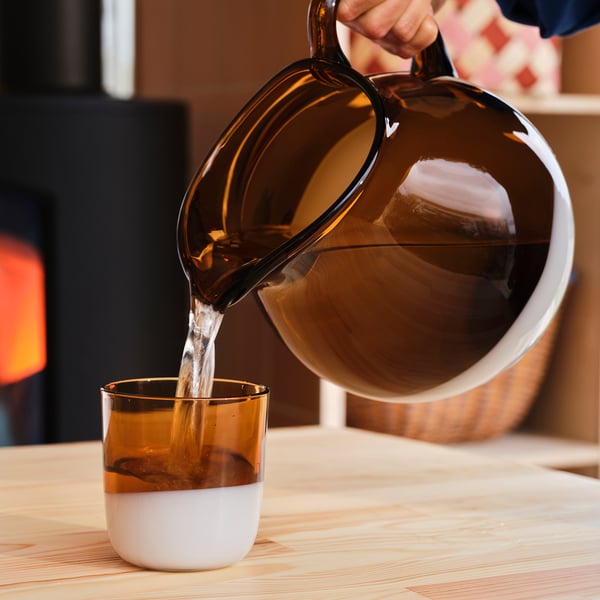 Pouring dark liquid from brown glass pitcher into two-toned glass cup.