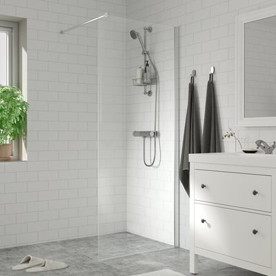 Modern bathroom with white tiles, glass shower, chrome fixtures, grey towels, small sink, mirror, and plant.