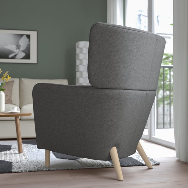 Modern grey wing chair with wooden legs in cosy room, providing comfort with high backrest and armrests.