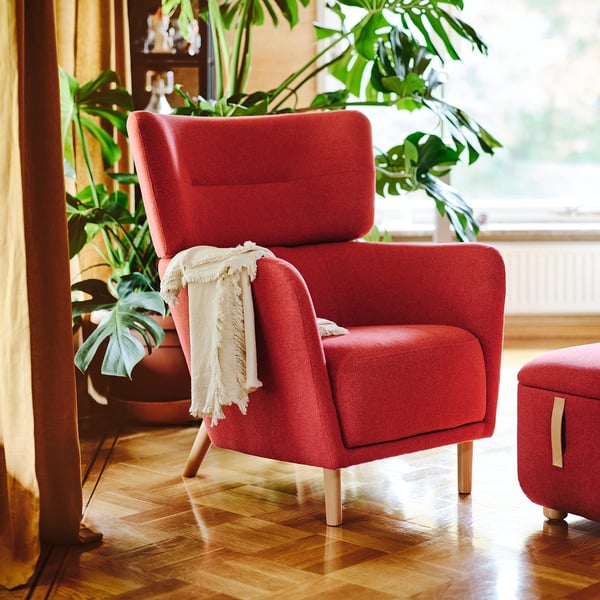 Red OSKARSHAMN armchair with wooden legs, white throw, plants.