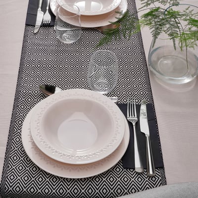 Elegant table setting with white plates and bowls, silverware, glasses on patterned placemats.