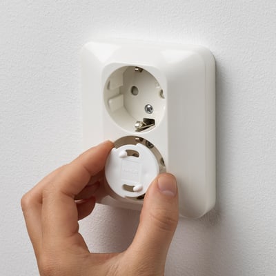 Hand holding a white safety plug, removing it from a wall socket to showcase childproofing.