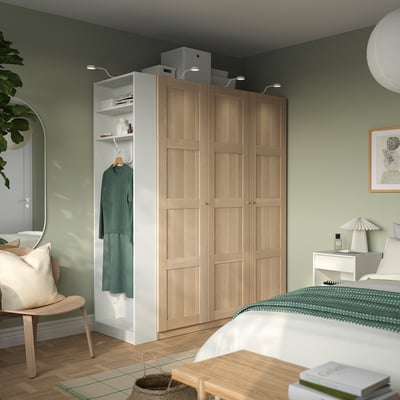 Modern bedroom with light wood wardrobe, storage, light, white dresser, green bedding, mirror.