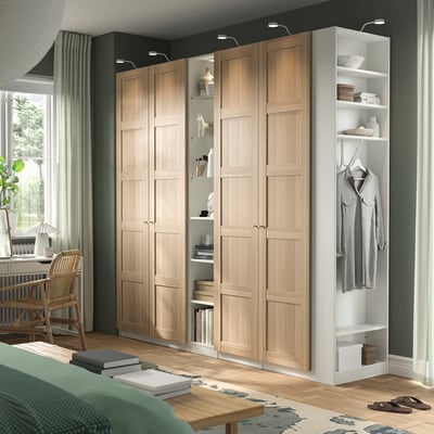 Beige PAX wardrobe with shelves and hanging space, tall, beside white bookshelf, spacious bedroom with wicker chair and green bed.