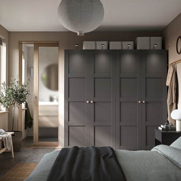 Modern bedroom featuring dark grey PAX wardrobe with sleek design, including mirrors, storage boxes, and a hanging plant for decoration.