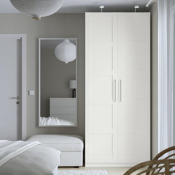 Modern bedroom with tall white PAX wardrobe, mirror, and seating area.