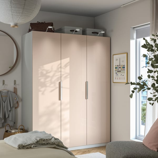 Modern bedroom with light PAX wardrobe, mirror, hooks, large window, and cosy chair with blanket.