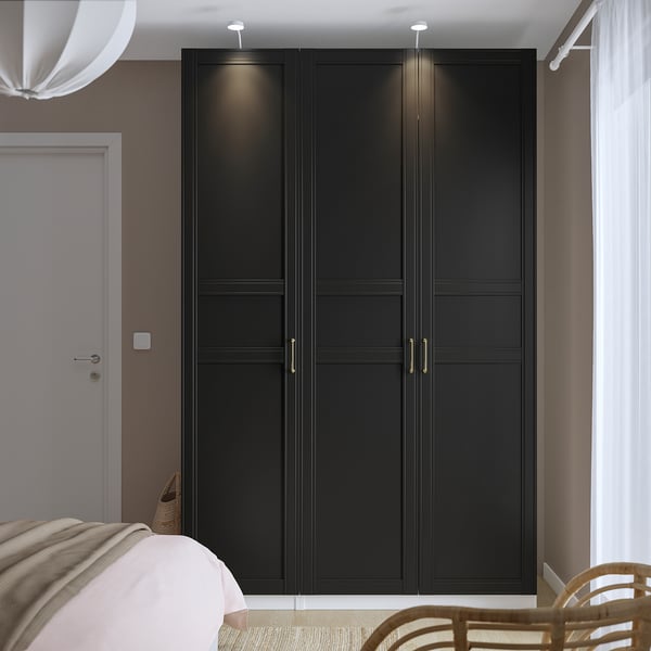 Large dark PAX wardrobe in bedroom, near door, beside partially visible bed, with wicker chair.