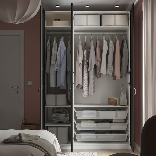 Open wardrobe displaying clothes, folded items in mesh baskets, and storage boxes. Fabric lamp hangs above.