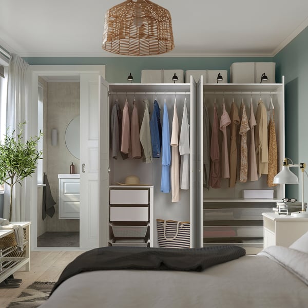 Modern bedroom with built-in wardrobe, clothes hanging, baskets, and a pendant light.