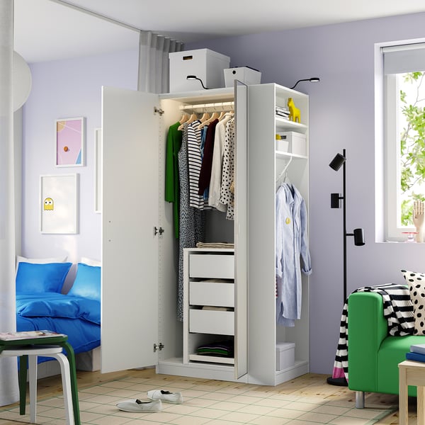 Open white wardrobe displaying clothes, drawers, and storage boxes in a colourful, organised room.