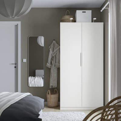 Minimalist bedroom with white PAX wardrobe, large mirror, and wicker baskets. Dark grey bedding completes the modern decor.