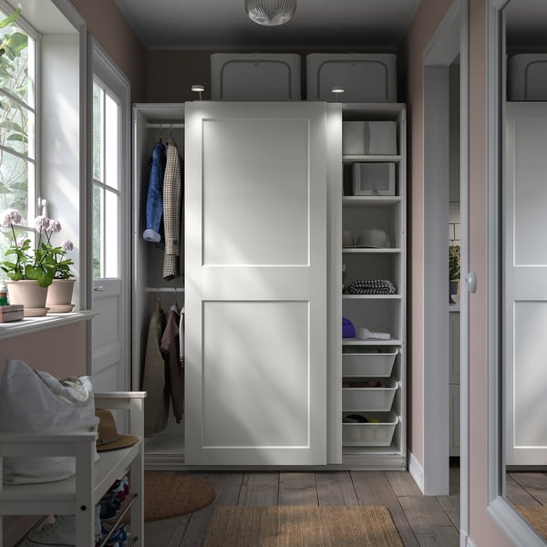 Modern white PAX wardrobe with sliding doors, open shelf, and organised storage baskets.