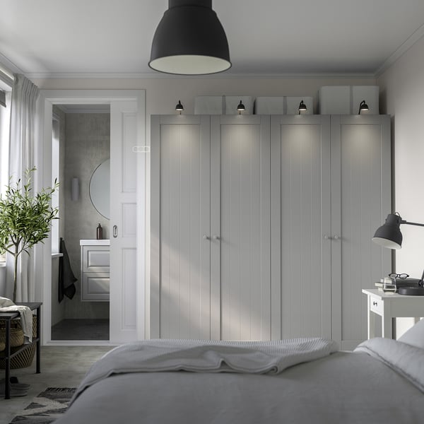 Minimalist bedroom with tall grey PAX wardrobe next to bathroom, featuring soft lighting and sleek design.
