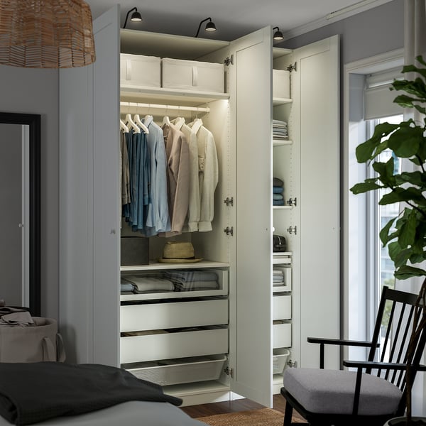 An open wardrobe with clothes on hangers, drawers, and shelves. Led lights illuminate the interior. The wardrobe is part of the PAX system.