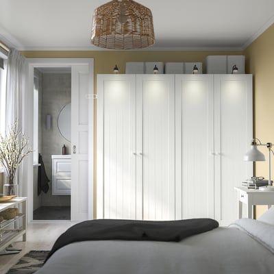 Modern bedroom with large PAX wardrobe, integrated lighting, rattan pendant, cosy bed, and partial view of bathroom.