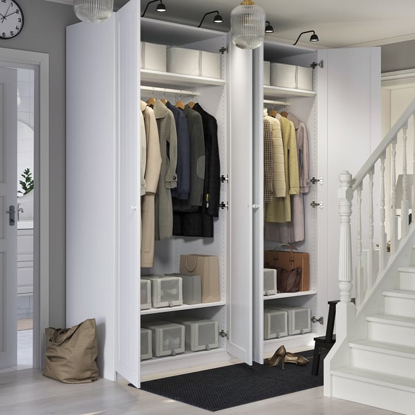 Open white closet with clothes and storage boxes. Floor lamp above, stairs on right, entrance door left, black mat below.