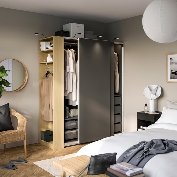 Bedroom with PAX wardrobe showing hanging clothes, shelves with accessories, and sliding doors.