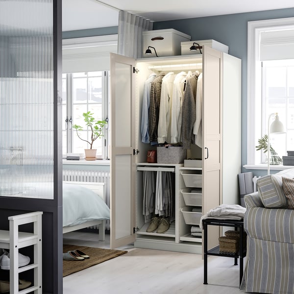 White PAX wardrobe with mirrored doors, clothes, and storage in cosy bedroom with blanket chair by window.
