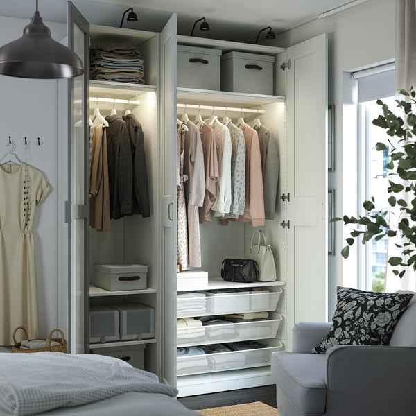 Bedroom with open PAX wardrobe showcasing clothes, folded items, and organisers. Interior lights on, with mirror doors reflecting space.