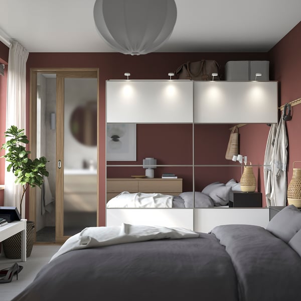 Modern bedroom a white PAX wardrobe with sliding doors, grey bedding, and red walls. Plants and decorative items enhance the space.