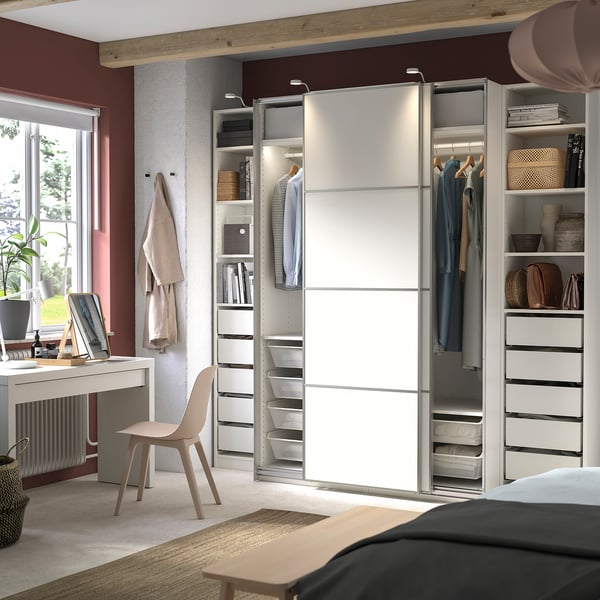 Modern bedroom with white PAX wardrobe, sliding doors, clothes, and desk with chair.