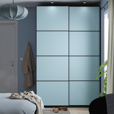 Large modern blue PAX wardrobe with sliding doors against a blue wall in a stylish bedroom.