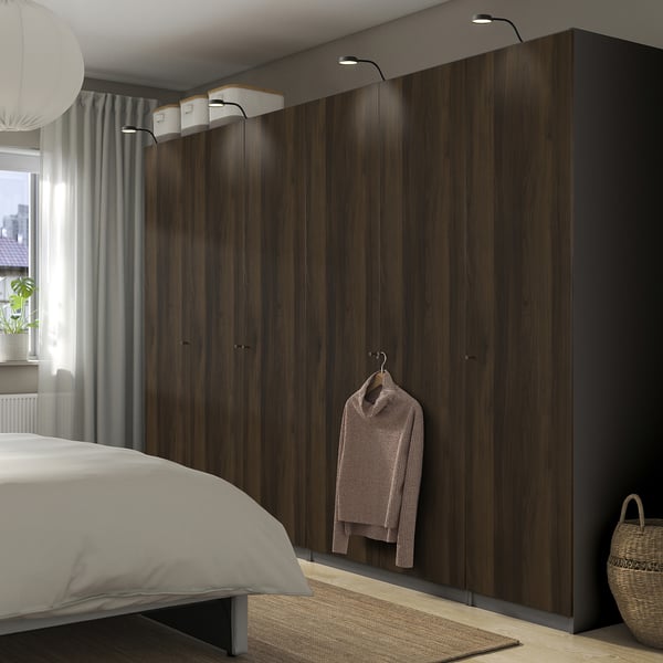 Modern bedroom with large dark wood PAX wardrobe. Wardrobe hanging lights and hanging sweater. Wardrobe is larger than bed, with bed near window.