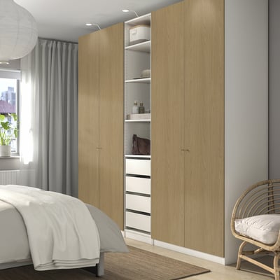 Modern bedroom with PAX wardrobe, open storage, wicker chair by window.