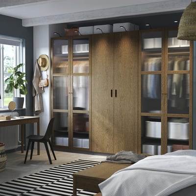 Modern bedroom with large wooden PAX wardrobe and black chair. Wardrobe glass and wooden doors, larger than bed and window.