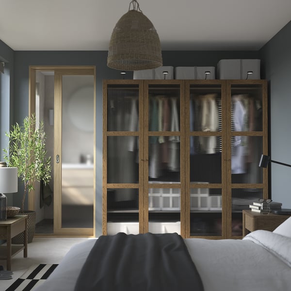 Beige PAX wardrobe, dark blue wall, glass doors. Modern bedroom with hanging lamp, plant, minimalist bed.