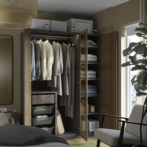 Wooden wardrobe with glass door hanging clothes, folded towels, and mesh baskets. It includes interior lighting and adjustable shelves.