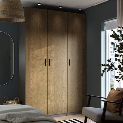 Large wooden PAX wardrobe against dark blue wall. Mirrors on left, chair right. Light wood floor.