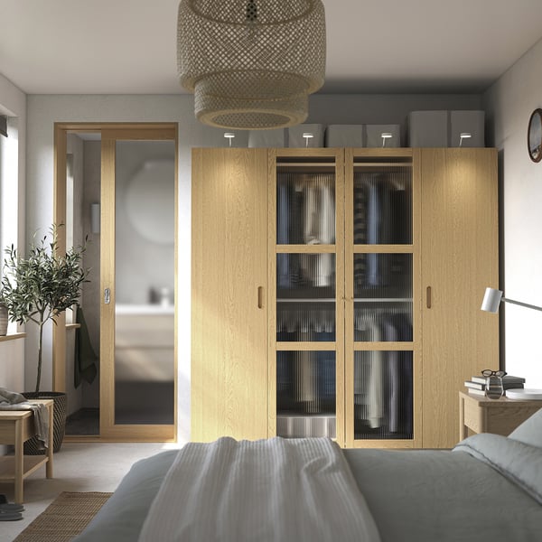 Modern bedroom with large PAX wardrobe, grey bed, plant, and pendant light. Wardrobe with glass doors and grey boxes.