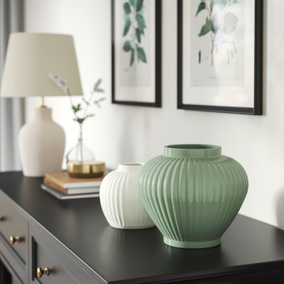 Grey-green PELARBJÖRK vases on black shelf with books, lamp, and gold decor. Larger green vase contrasts with smaller white one.