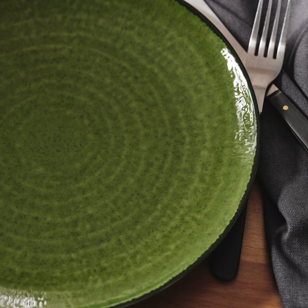 Close-up of glossy, green textured stoneware plate with dark rim, and part of fork and grey napkin.