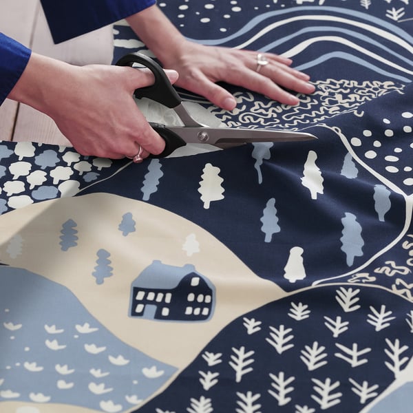 Cutting patterned fabric with scissors. Blue and beige mountain design, ideal for sewing crafts or home accents.