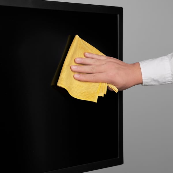 Hand with yellow cloth cleaning black surface, ensuring shiny, streak-free result.