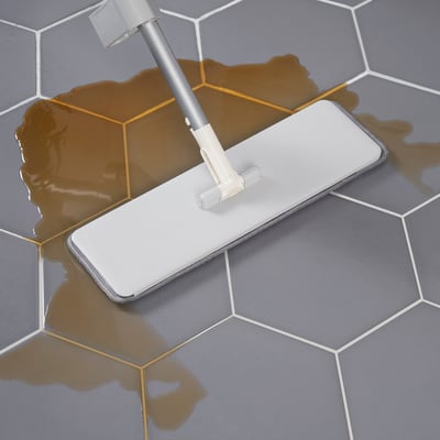 A flat mop with a microfiber cloth cleaning a tiled floor. The cloth absorbs liquid efficiently, making cleaning easier.