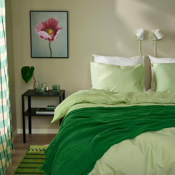 Cozy bed with green duvet, white pillows, pink flower art, and striped curtains.