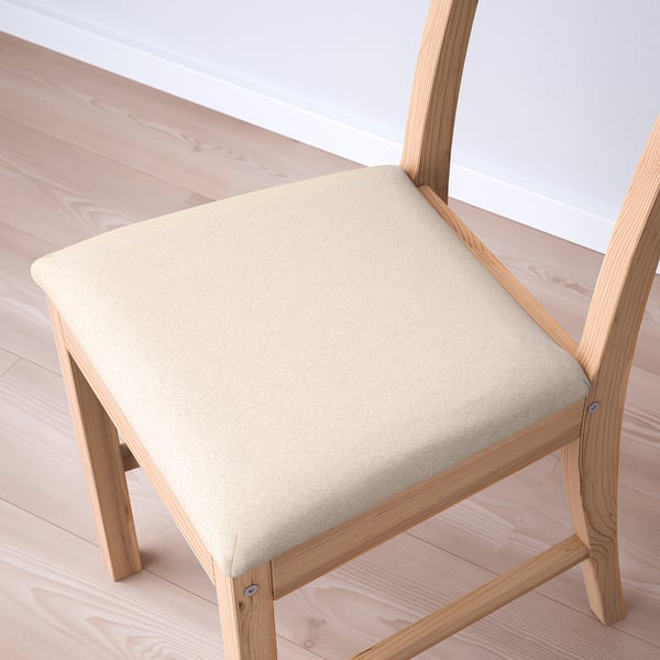 Modern angled wooden chair with soft, beige upholstered seat, set on light wood floor.